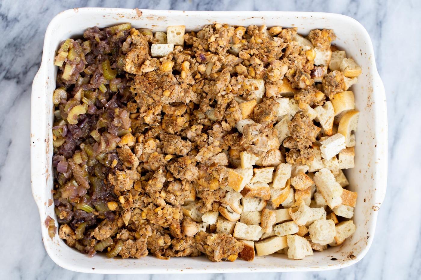 vegan stuffing being tossed in a white casserole dish