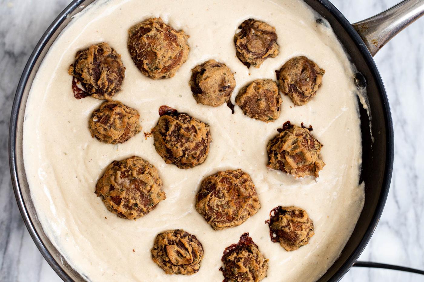 vegan mushroom balls being added to gravy in a saucepan