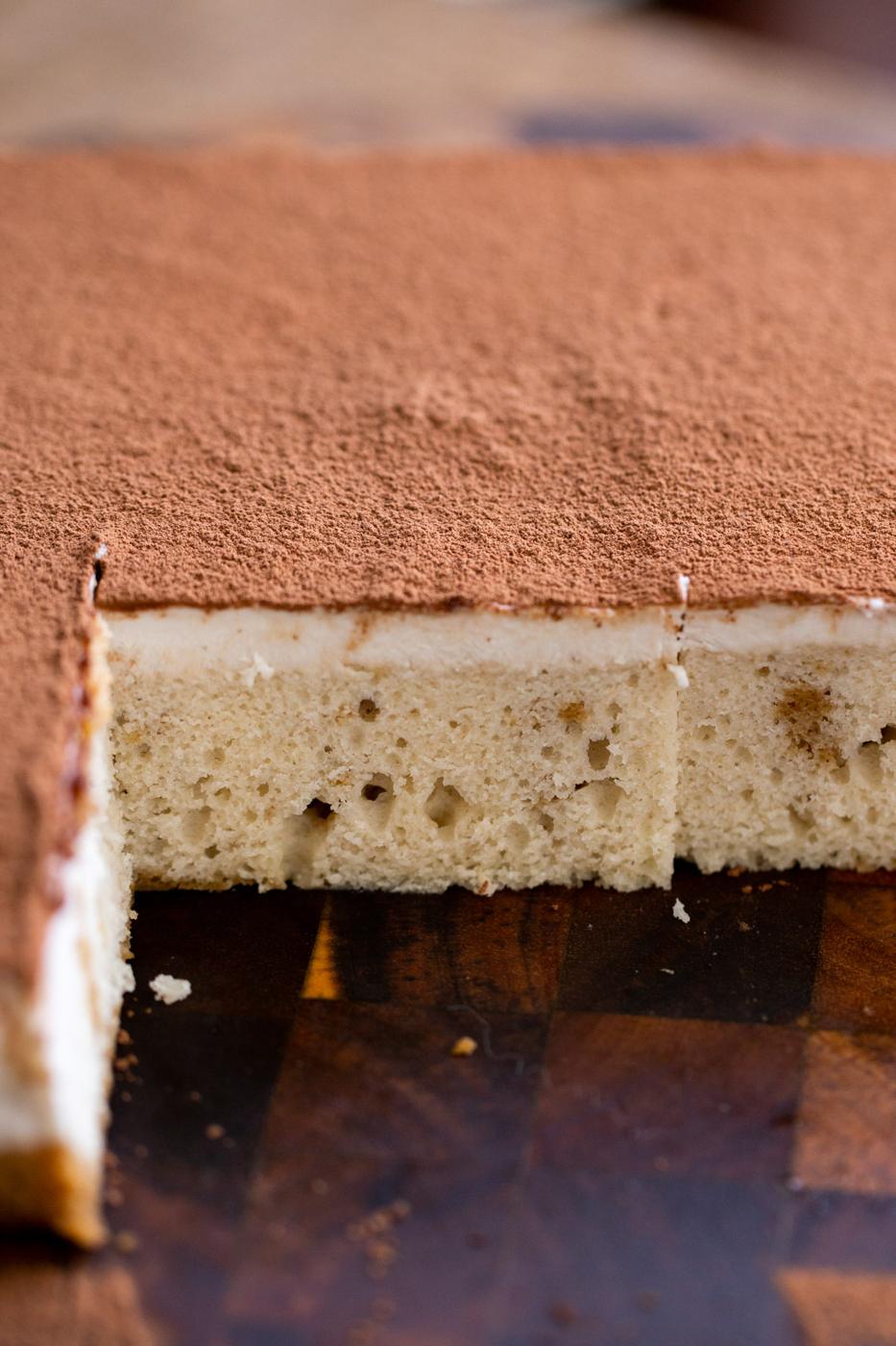 vegan tiramisu sheet cake on a wooden board dusted with cocoa powder