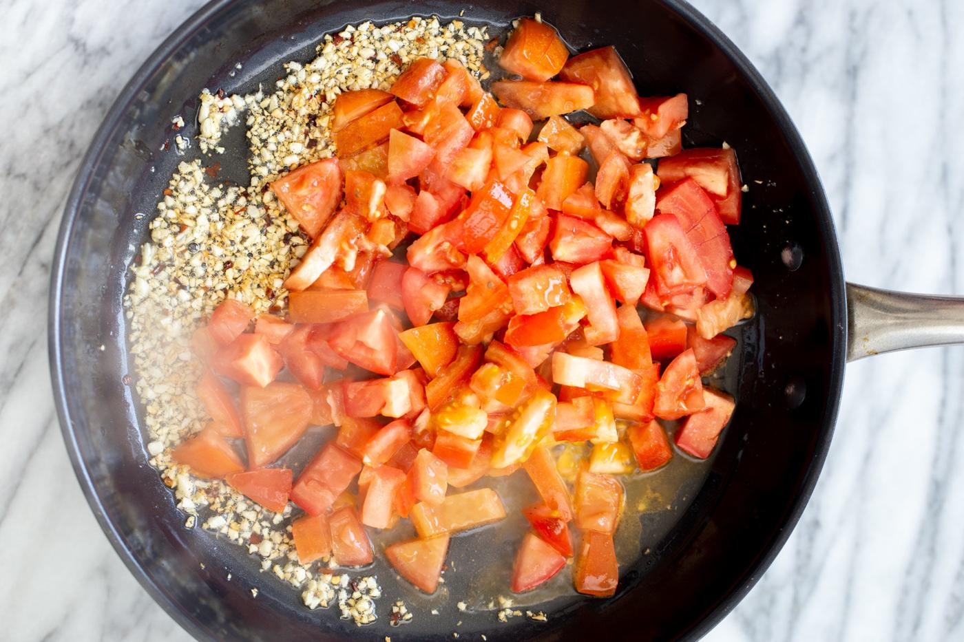 fresh tomato chunks being added to sauteed garlic and red pepper to make vegan tomato sauce