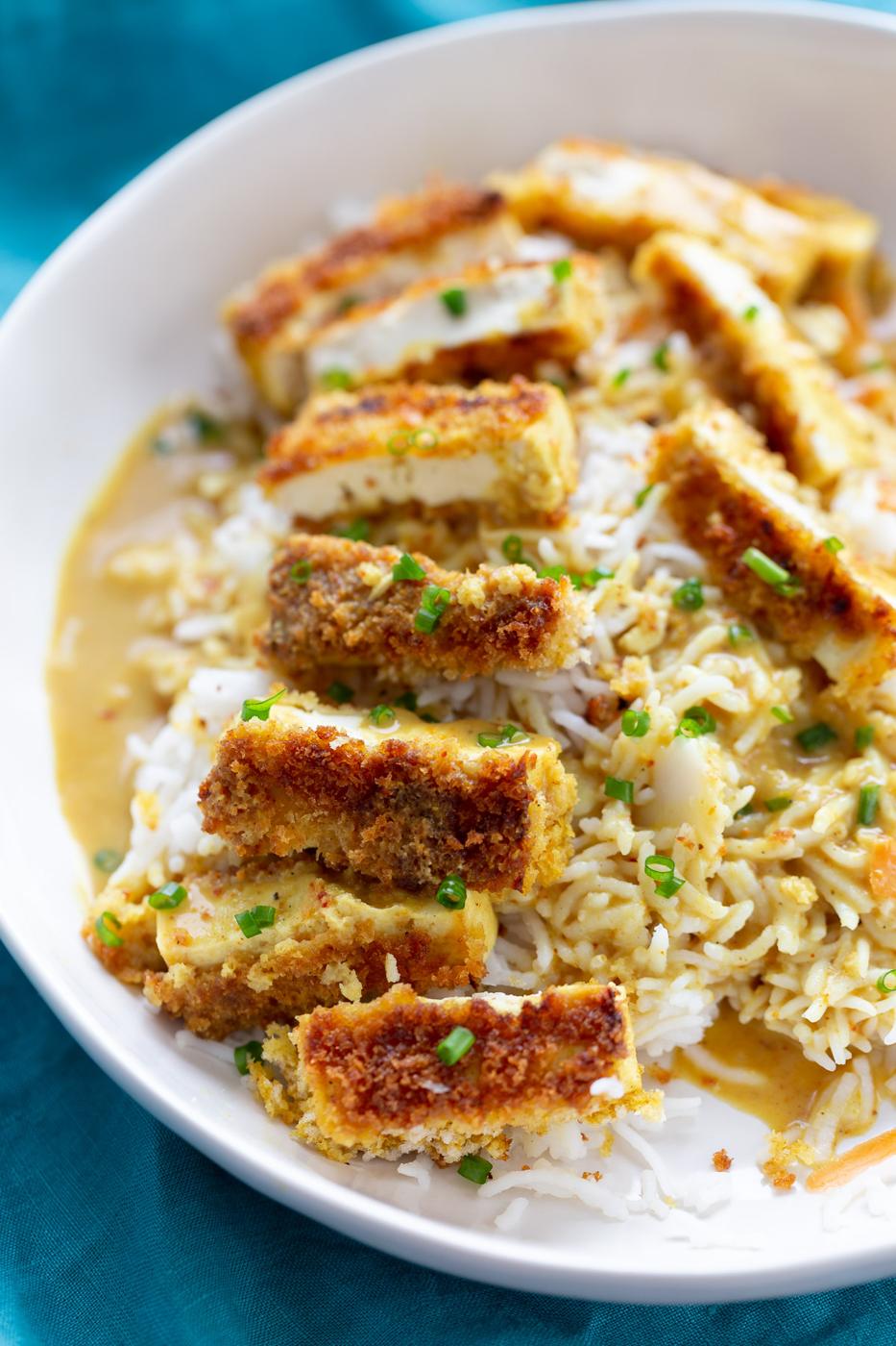 a bowl of rice topped with breaded pan-fried tofu slices and drizzled with Japanese curry sauce