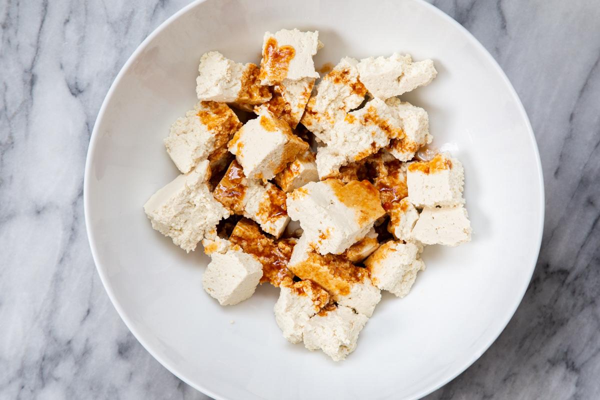 marinade being added to torn tofu chunks in a white bowl