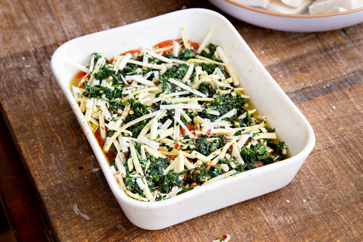 tofu and marinara sauce being topped with spinach and grated cheese