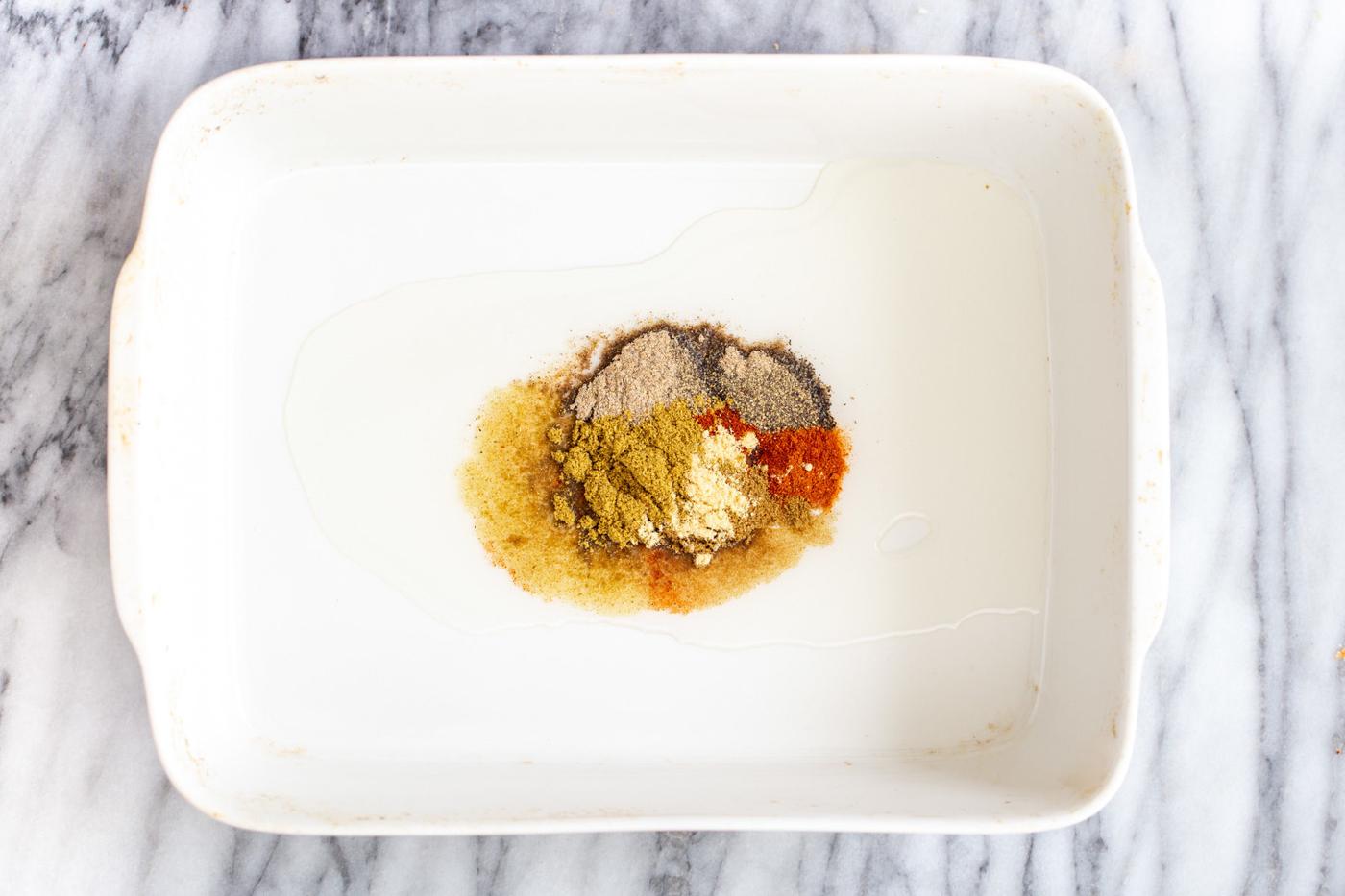 oil and indian spices in a white casserole dish