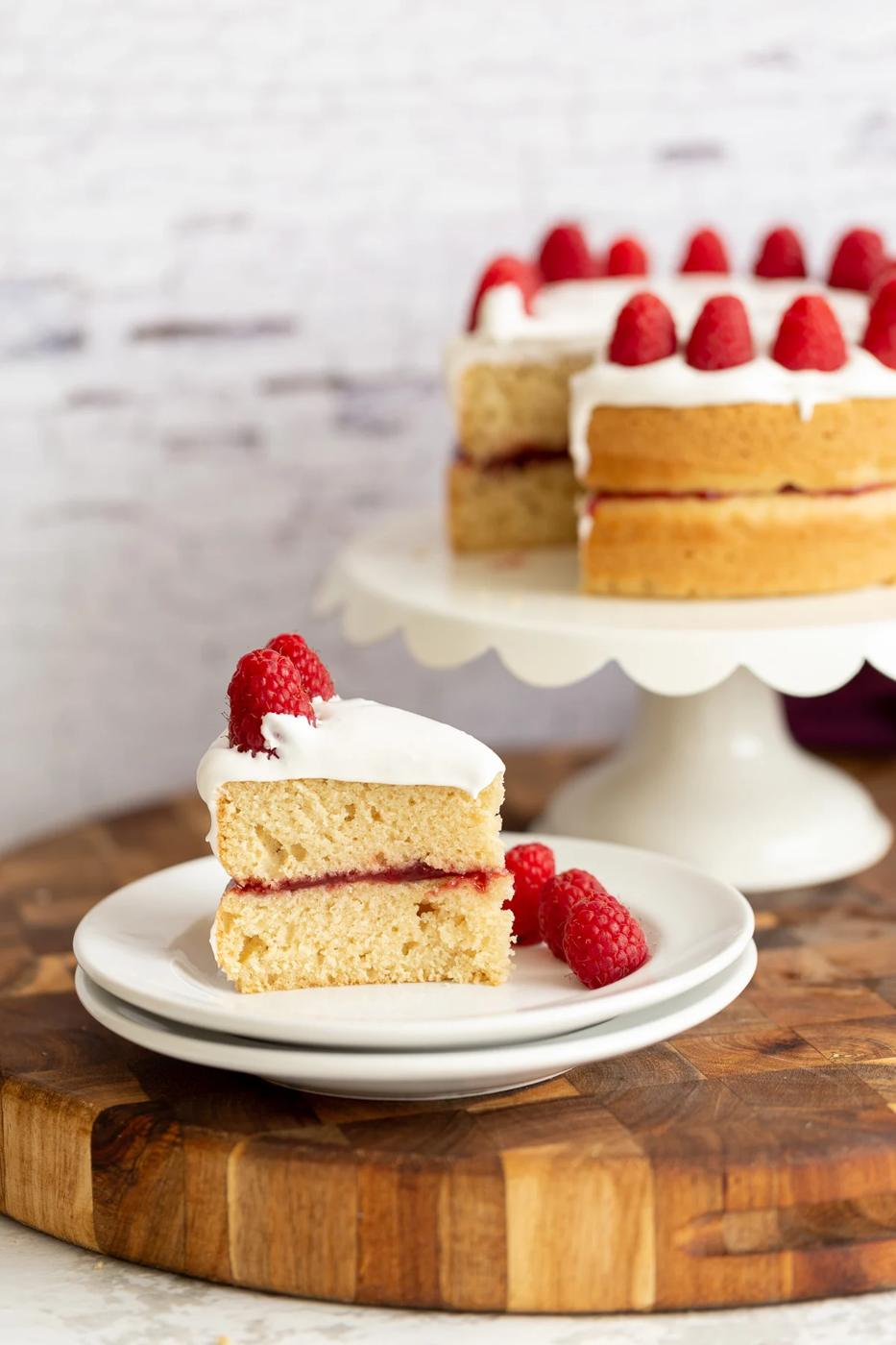 a slice of vegan white cake filled with raspberry preserves and topped with coconut whipped cream