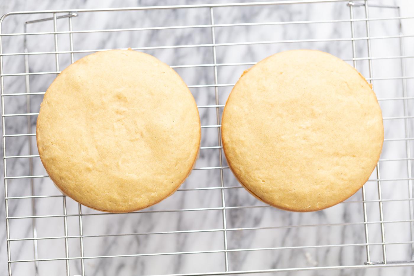 two vegan white cakes cooling next to each other on a cooling rack