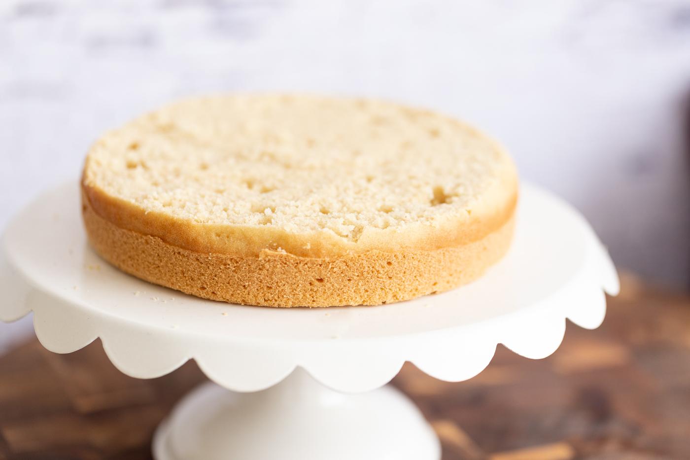 half a vegan white cake on a cake stand ready to be assembled into a layer cake