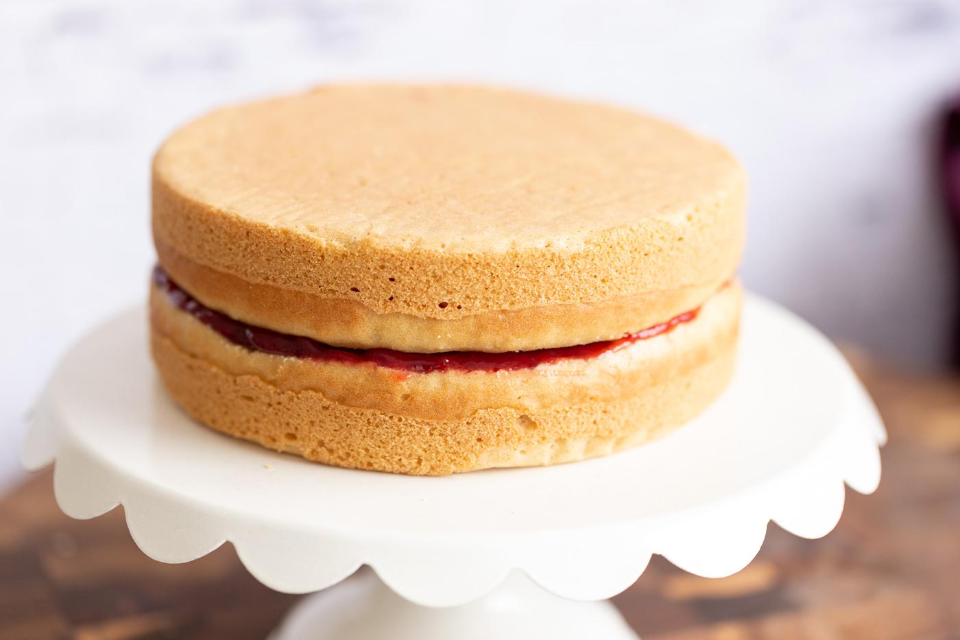 assembled vegan white cake filled with raspberry jam on a cake stand
