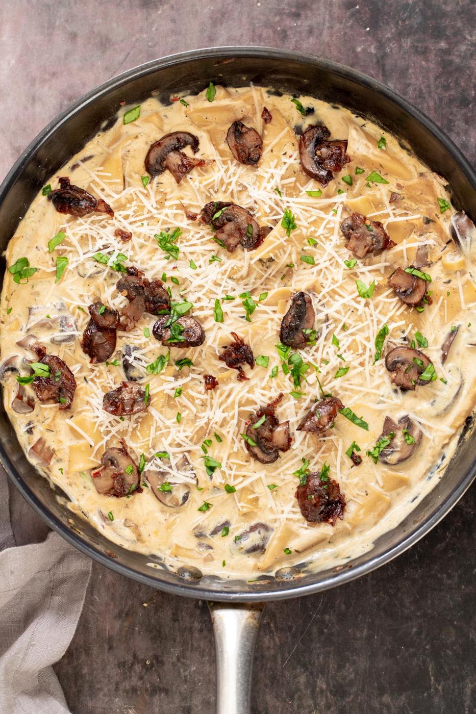 vegan parmesan cheese being sprinkled on top of a vegan white skillet lasagna with balsamic mushrooms