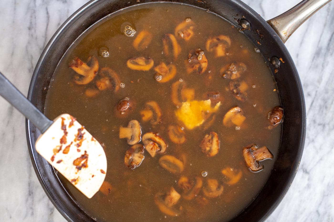 broth being added to sauteed mushrooms in a skillet