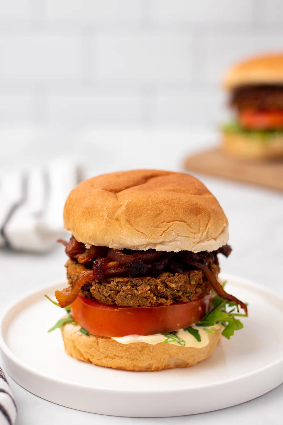 side view of a Middle Eastern Za'atar spiced chickpea burger with caramelized onion and hummus on a white plate