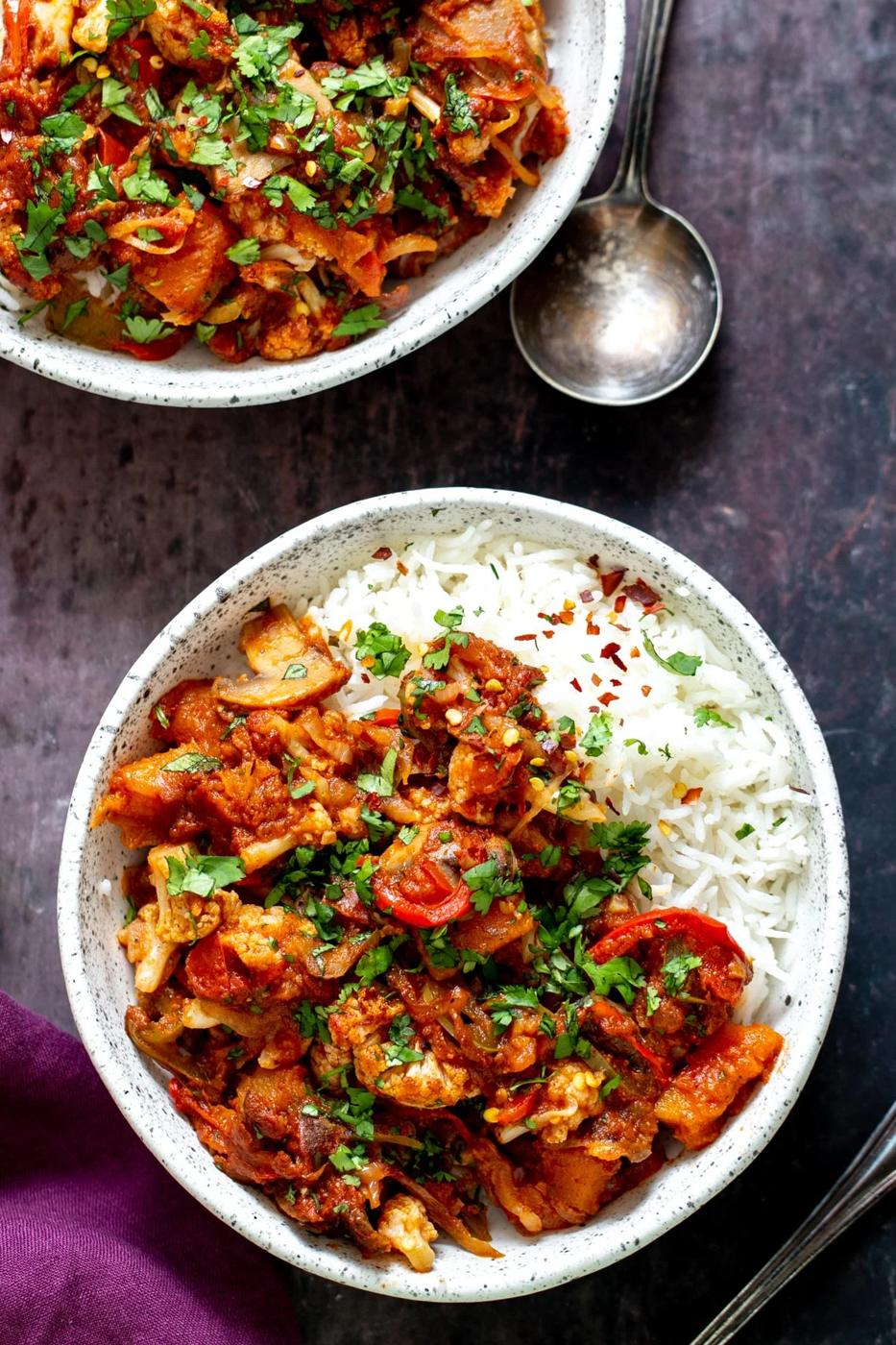a bowl of vegetable balti served with rice and sprinkled with fresh parsley