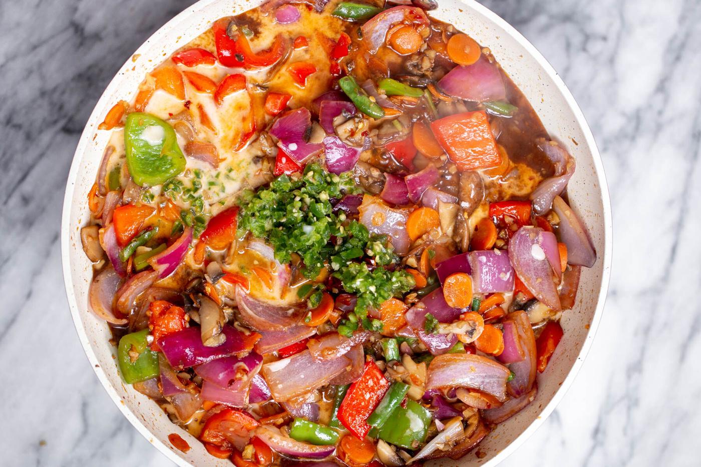 minced green chili being added to a saucepan with vegetables and sweet and sour sauce