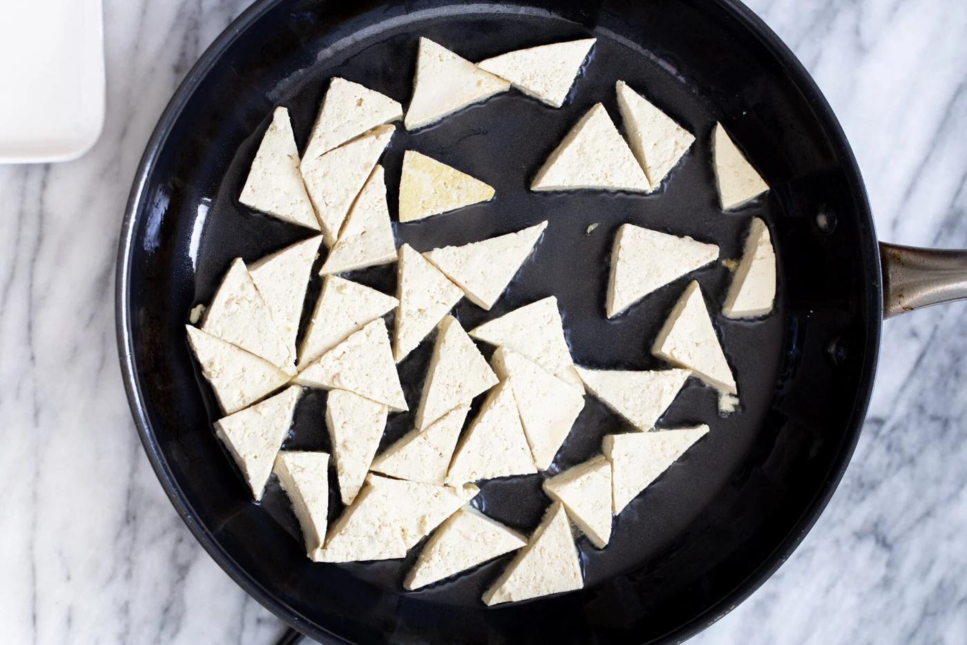 pressed tofu triangles being added to a black skillet