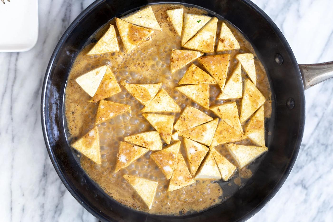 curry sauce being added to saucepan to coat pan-fried tofu