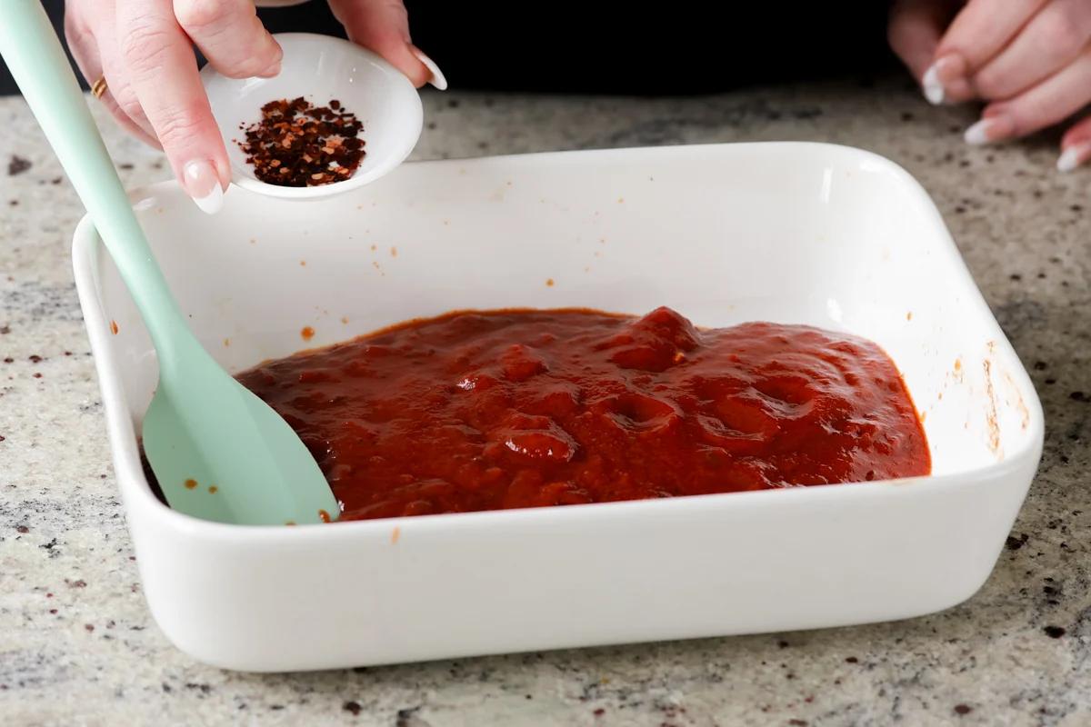 adding seasoning to the pasta sauce in the baking pan