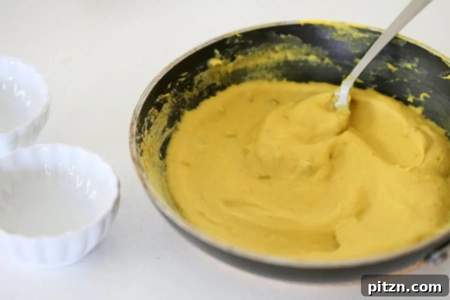 Preparing the Vegan Cheese Ball mixture in a skillet, showing the transformation from liquid to a thick, custardy consistency. Nut-free, dairy-free, and gluten-free cheddar alternative.