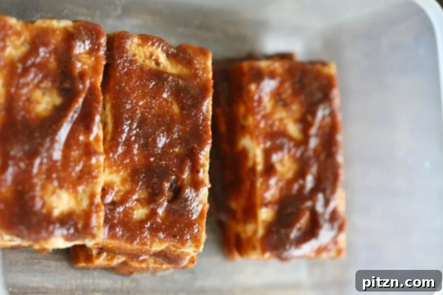 Tofu strips being brushed with a flavorful marinade, preparing them for breading and cooking.
