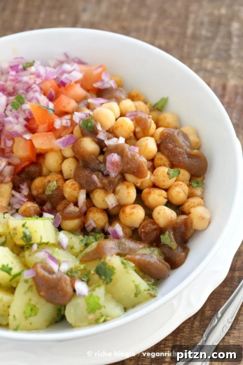 Zesty Chickpea Potato Chaat Bowl with Date Tamarind Drizzle 4 A vibrant close-up of the Chickpea Aloo Chaat Bowl, showcasing the diverse ingredients like mint cilantro potatoes, spiced chickpeas, tamarind date chutney, onions, and tomatoes, all seasoned with chaat masala. Ideal for vegan and gluten-free diets. | VeganRicha.com #vegan #glutenfree #bowl #recipe