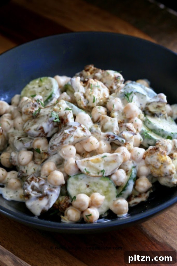 Close-up shot of Vegan Potato Salad with chickpeas and cauliflower in a black bowl, garnished with fresh herbs.