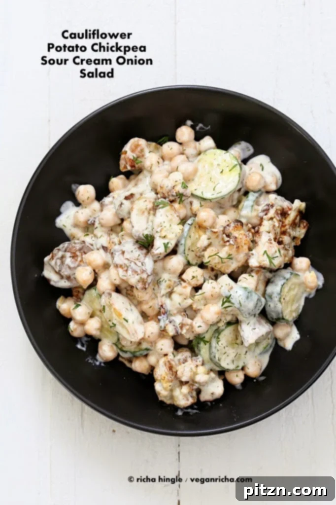 A large black bowl filled with Vegan Potato Salad, featuring roasted chickpeas, cauliflower, and zucchini, ready to be served.