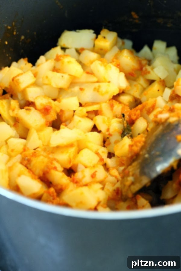 Cubed potatoes and salt being mixed into tomato gravy