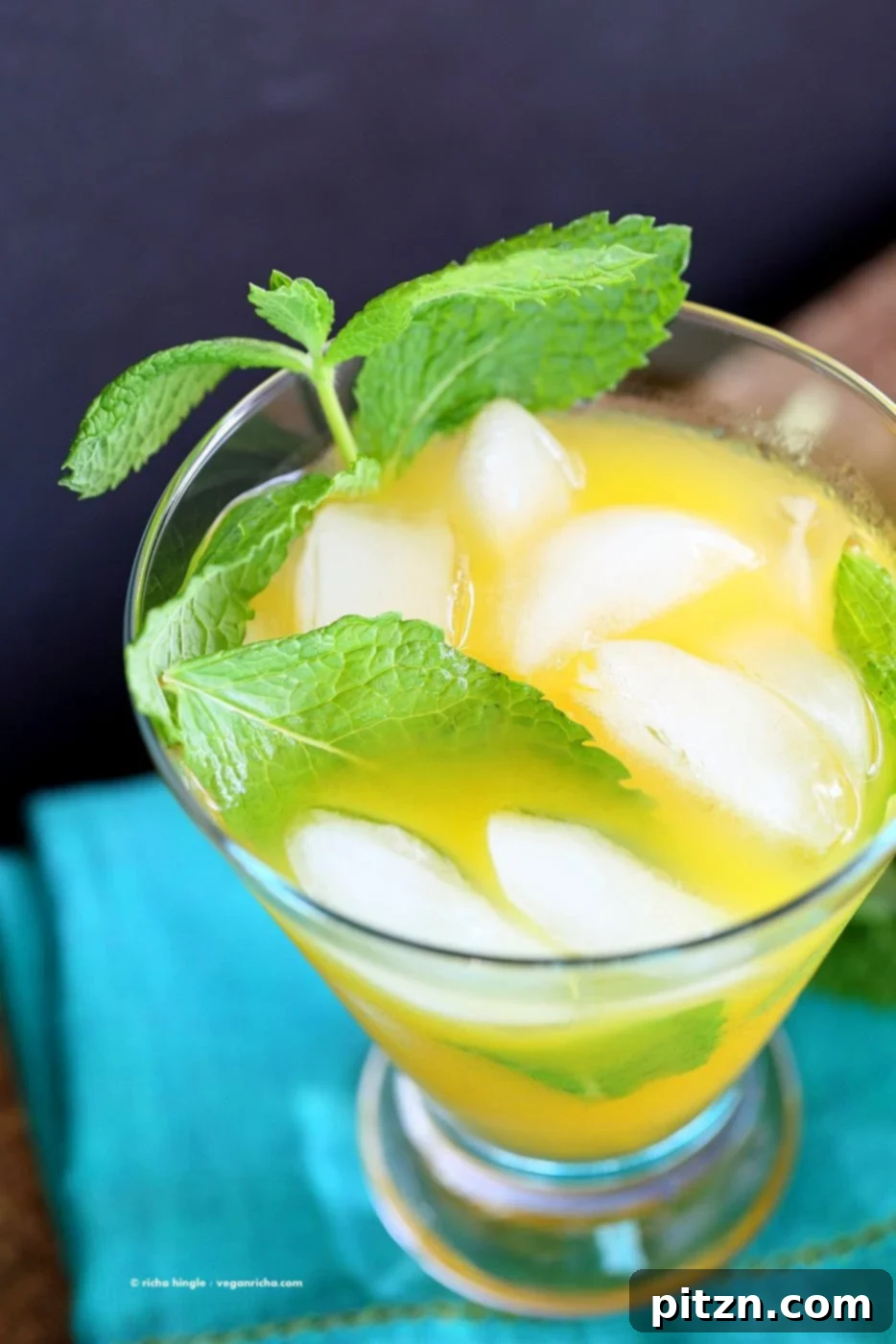 Close-up of a refreshing mango mojito with ice, mint leaves, and lime slices, showcasing its vibrant yellow color and inviting texture. This tropical drink is vegan and gluten-free.