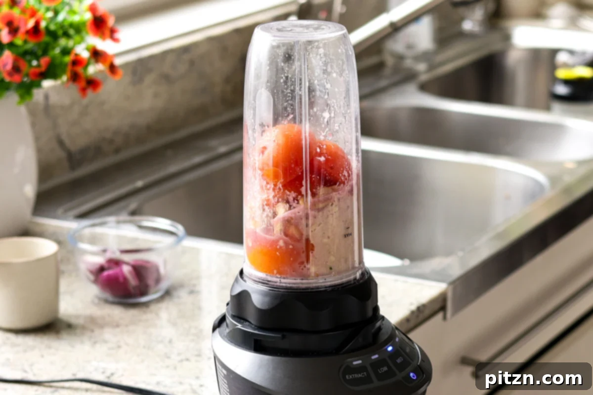 Adding tomatoes, cashews, and various spices to a blender, preparing for the creamy tomato base of the curry.