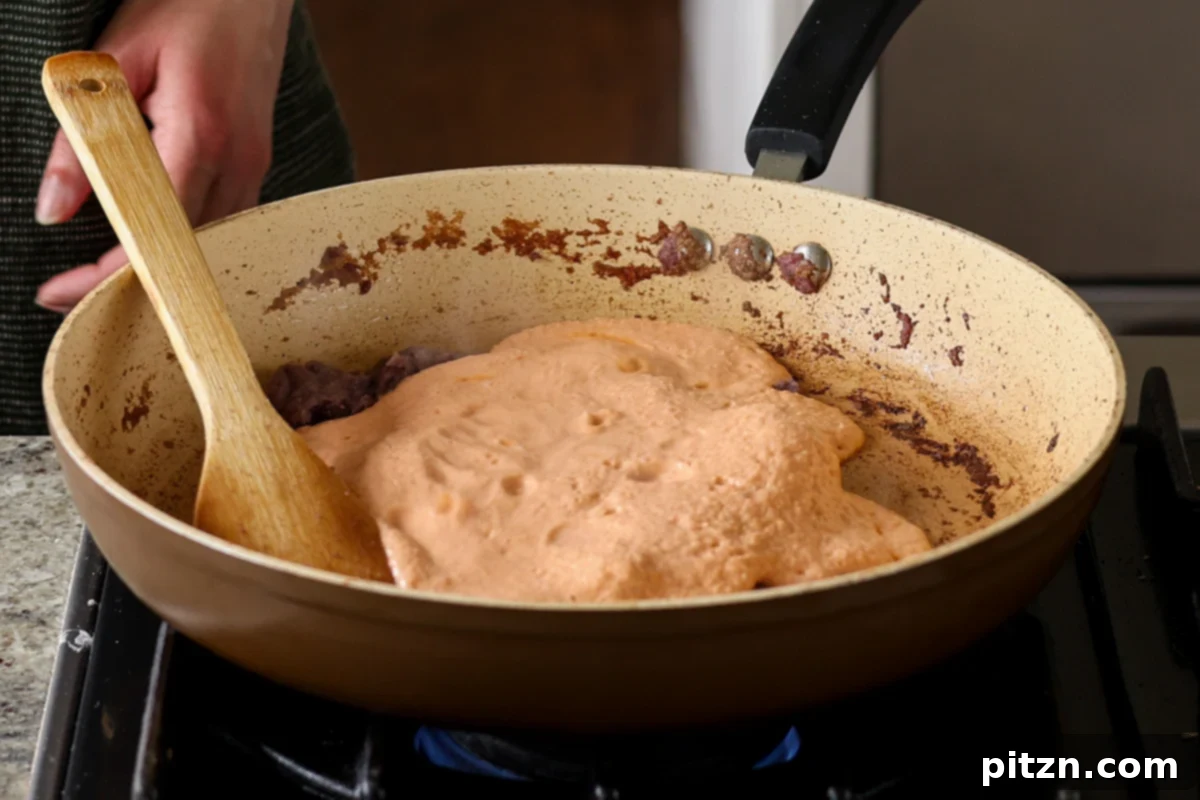 Adding the creamy tomato masala mixture to the skillet with the cooked aromatics, ready to be stirred and combined.