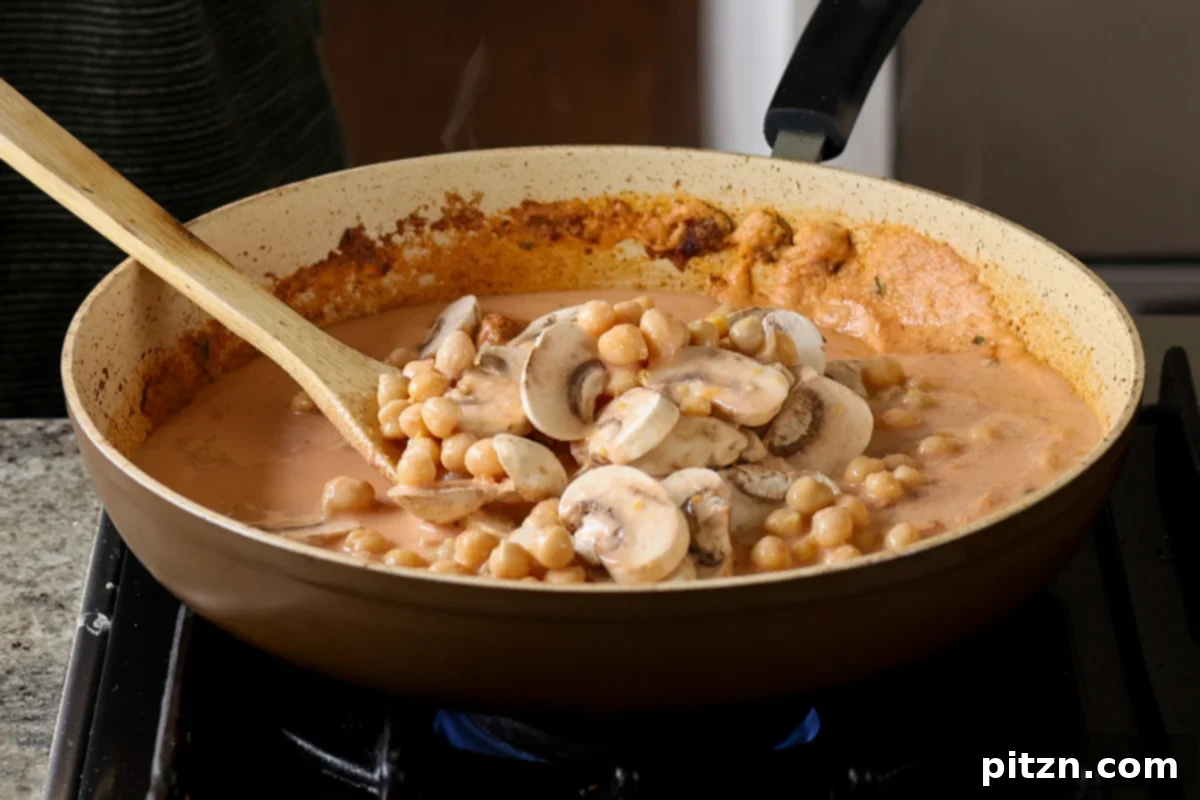 Adding chickpeas to the rich masala sauce in the pan, preparing for the next stage of cooking.