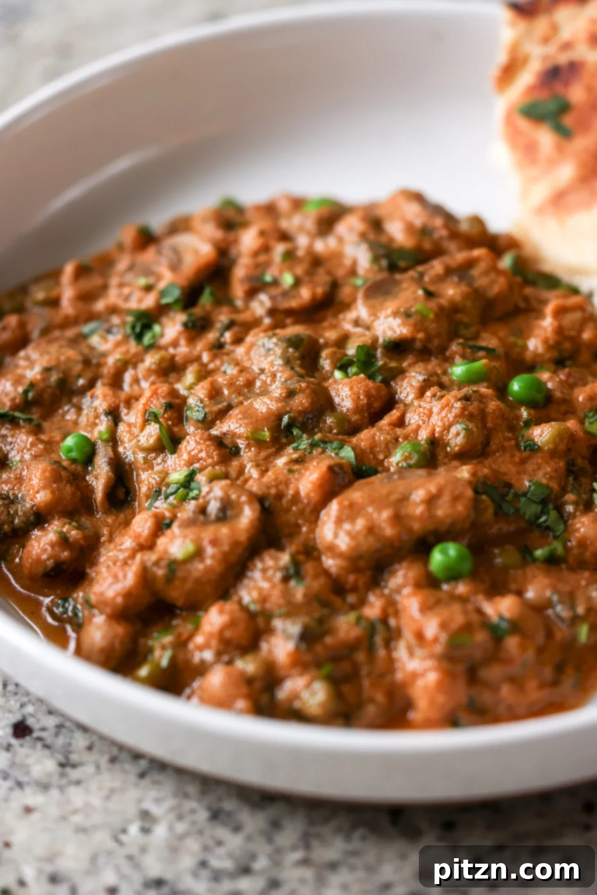 A serving of Mushroom Matar Masala in a bowl, accompanied by warm, fluffy flatbread, ready to be enjoyed.