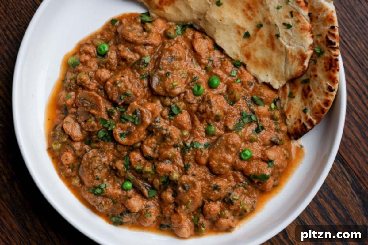 A generous serving of Mushroom Matar Masala in a bowl, with a piece of warm flatbread beautifully placed on the side, inviting a delightful meal.
