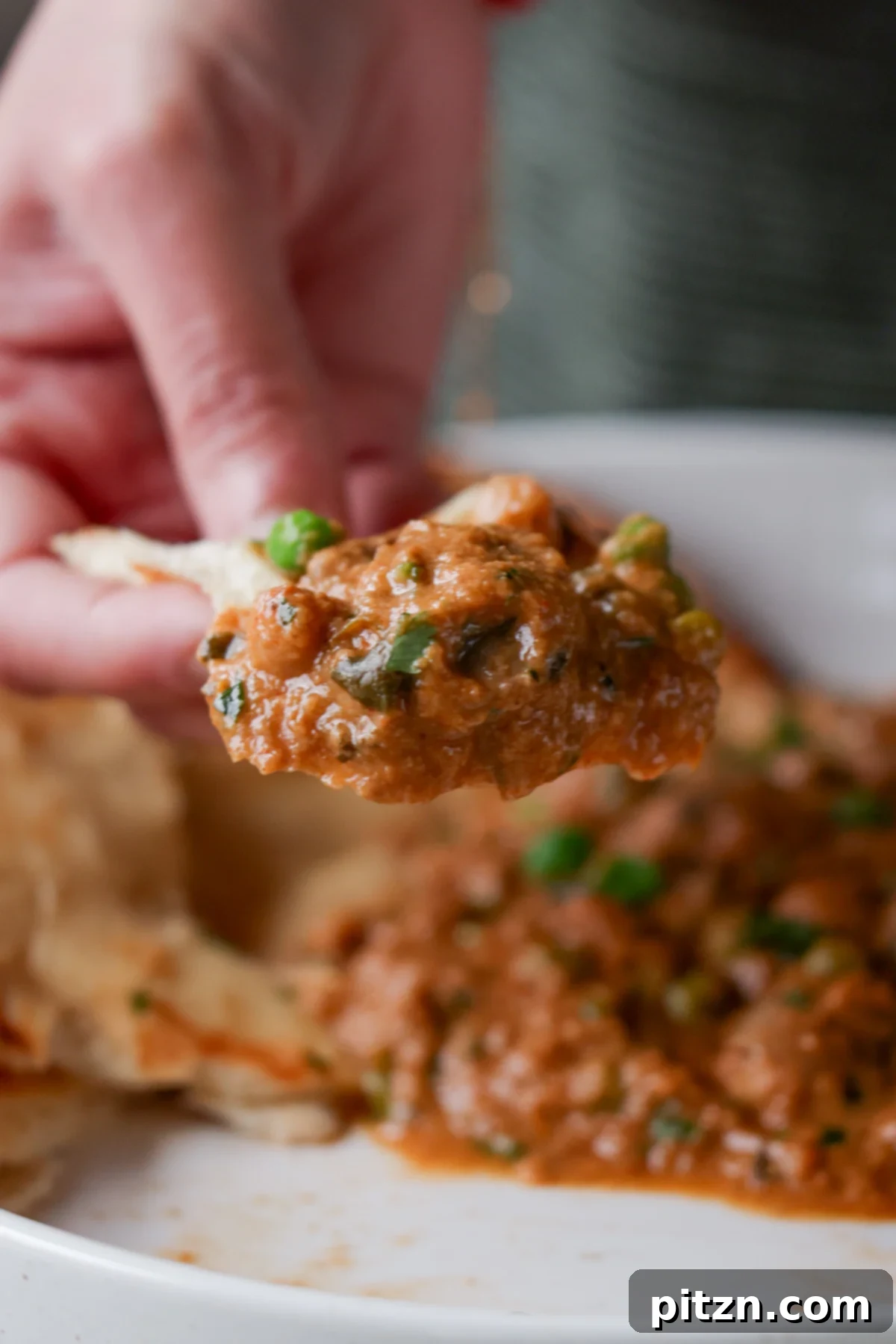 A hand scooping a generous portion of Mushroom Matar Masala onto a piece of warm flatbread, highlighting the rich texture of the curry.