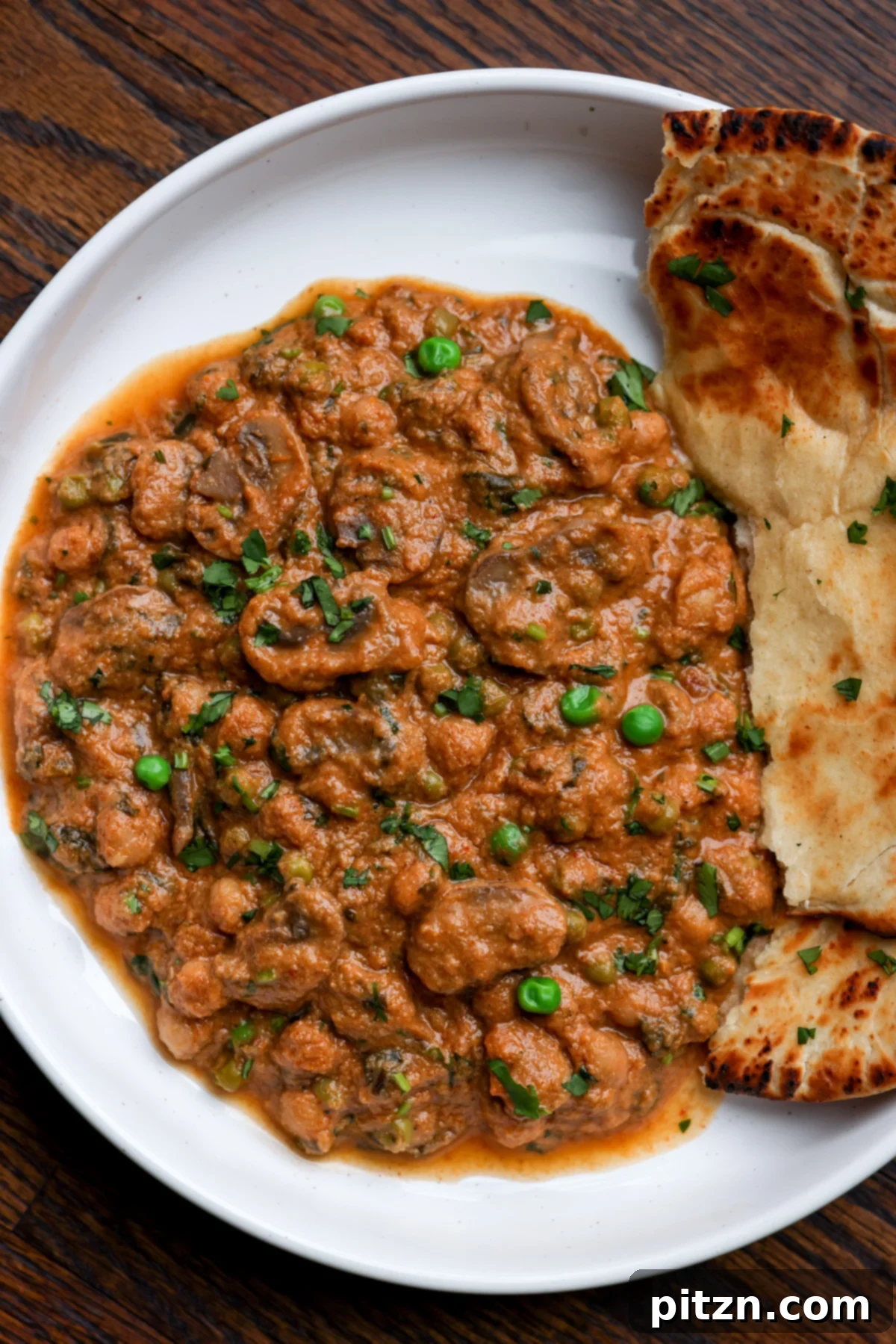 A beautifully presented bowl of Mushroom Matar Masala, garnished with fresh cilantro, alongside a stack of homemade flatbread.