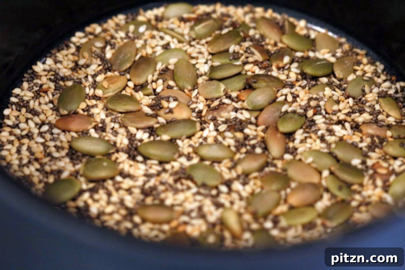 Seeded Ginger Chocolate No Bake Granola Bars 4 Process photo showing pumpkin and sesame seeds being toasted in a skillet for Super Seedy Chocolate No Bake Granola Bars. This step-by-step image illustrates the preparation of easy, healthy, vegan, gluten-free, and nut-free snack bars with candied ginger and gingerbread spices.
