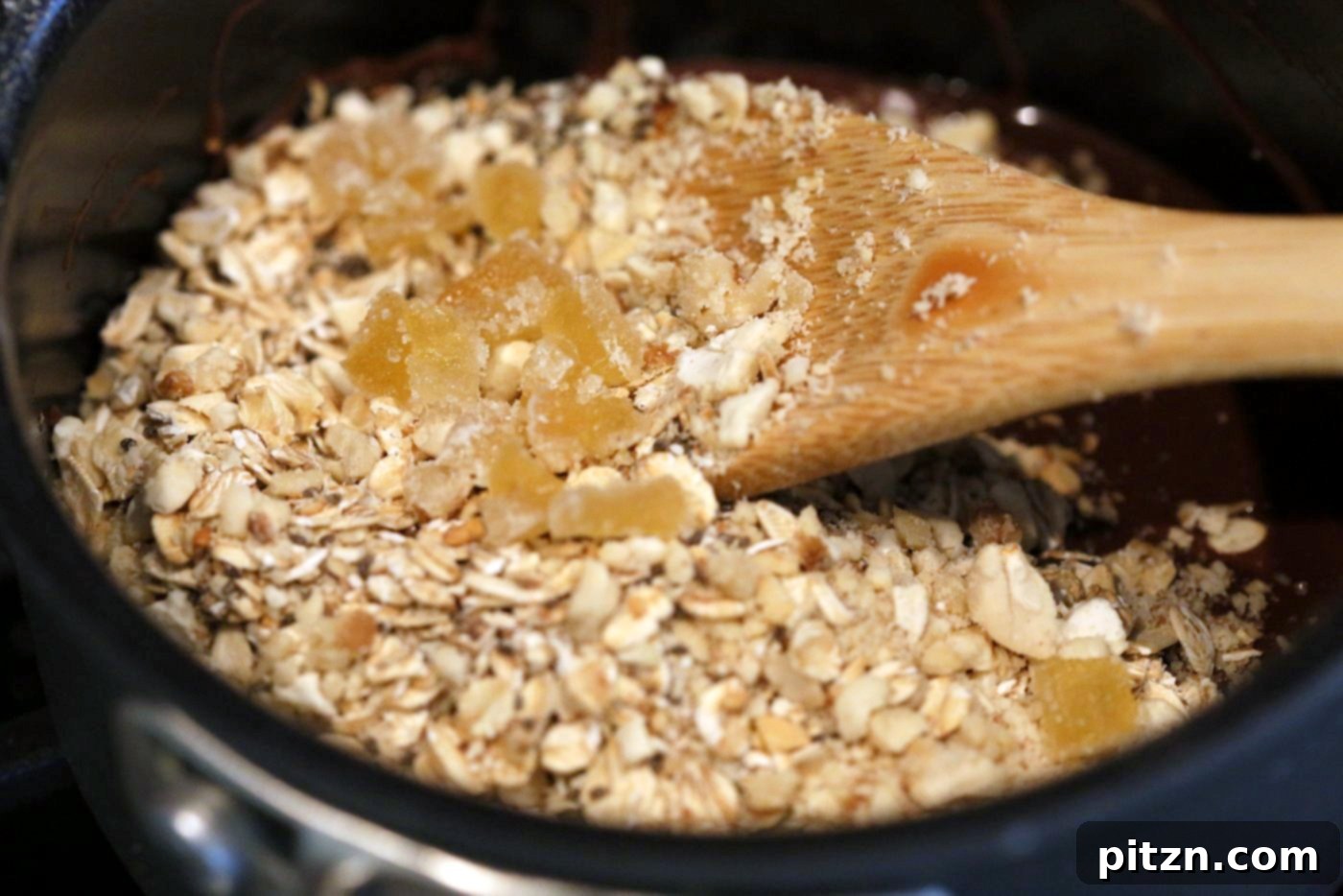 Seeded Ginger Chocolate No Bake Granola Bars 5 Process photo showing melted chocolate and nut butter being folded into a bowl of toasted oats, seeds, and nuts for Super Seedy Chocolate No Bake Granola Bars. This image demonstrates a key step in creating easy, healthy, vegan, gluten-free, and nut-free snack bars with candied ginger and gingerbread spices.