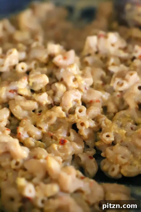 whole wheat elbow pasta being tossed with dairy-free cheese sauce to make vegan mac and cheese