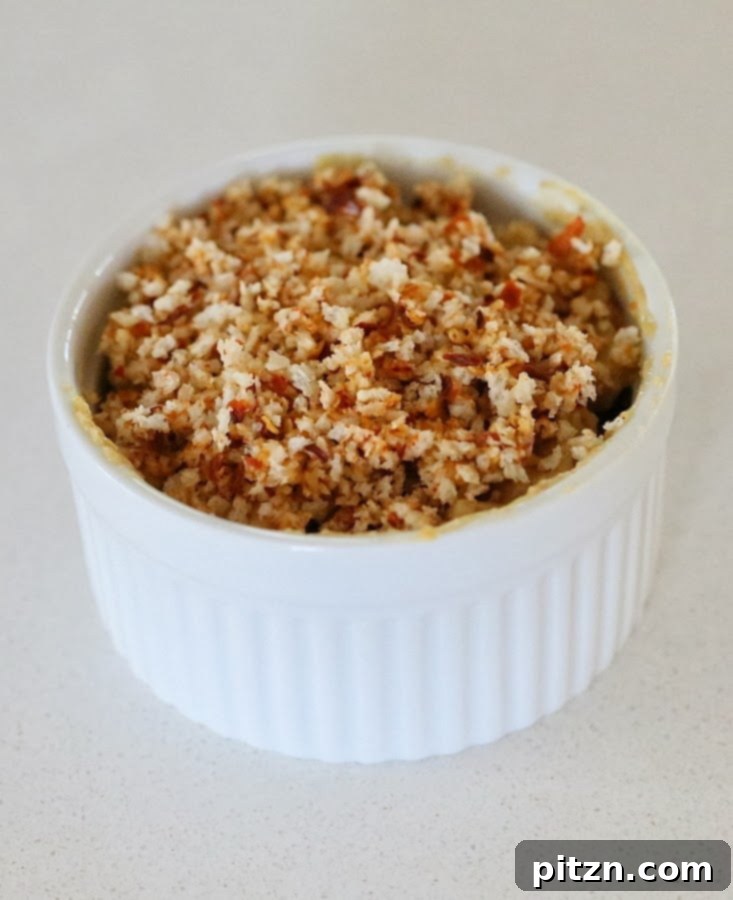 individual ramekins with dairy-free spicy mac and cheese being filled topped with vegan breadcrumbs 
