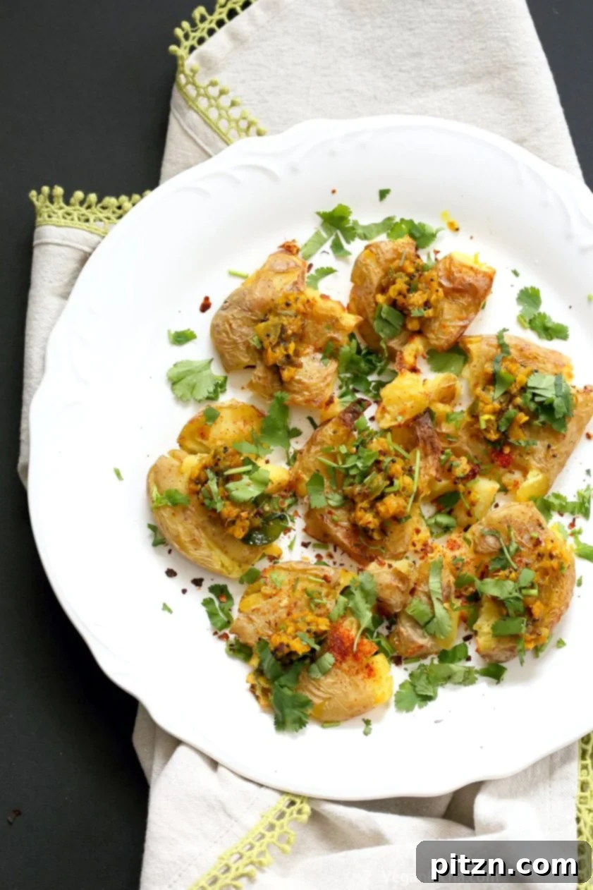 Spiced Smashed Potatoes with a Mustard Ginger Infusion 3 Close-up of golden-brown Indian Spiced Smashed Potatoes on a baking sheet, showcasing their crispy edges and fluffy interior. Topped generously with a vibrant mustard-ginger tempering and fresh cilantro.