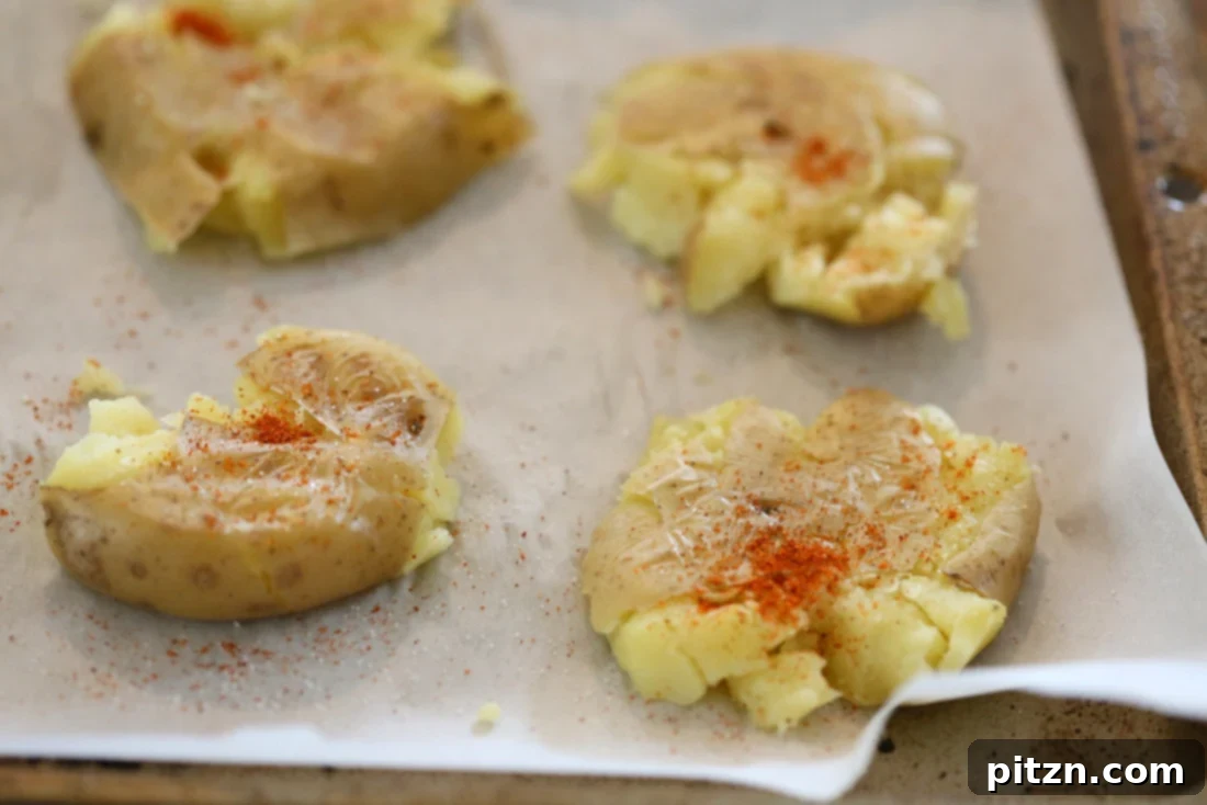 Spiced Smashed Potatoes with a Mustard Ginger Infusion 6 Cooked potatoes being smashed flat on a parchment-lined baking sheet, prepared for baking to achieve a crispy texture.
