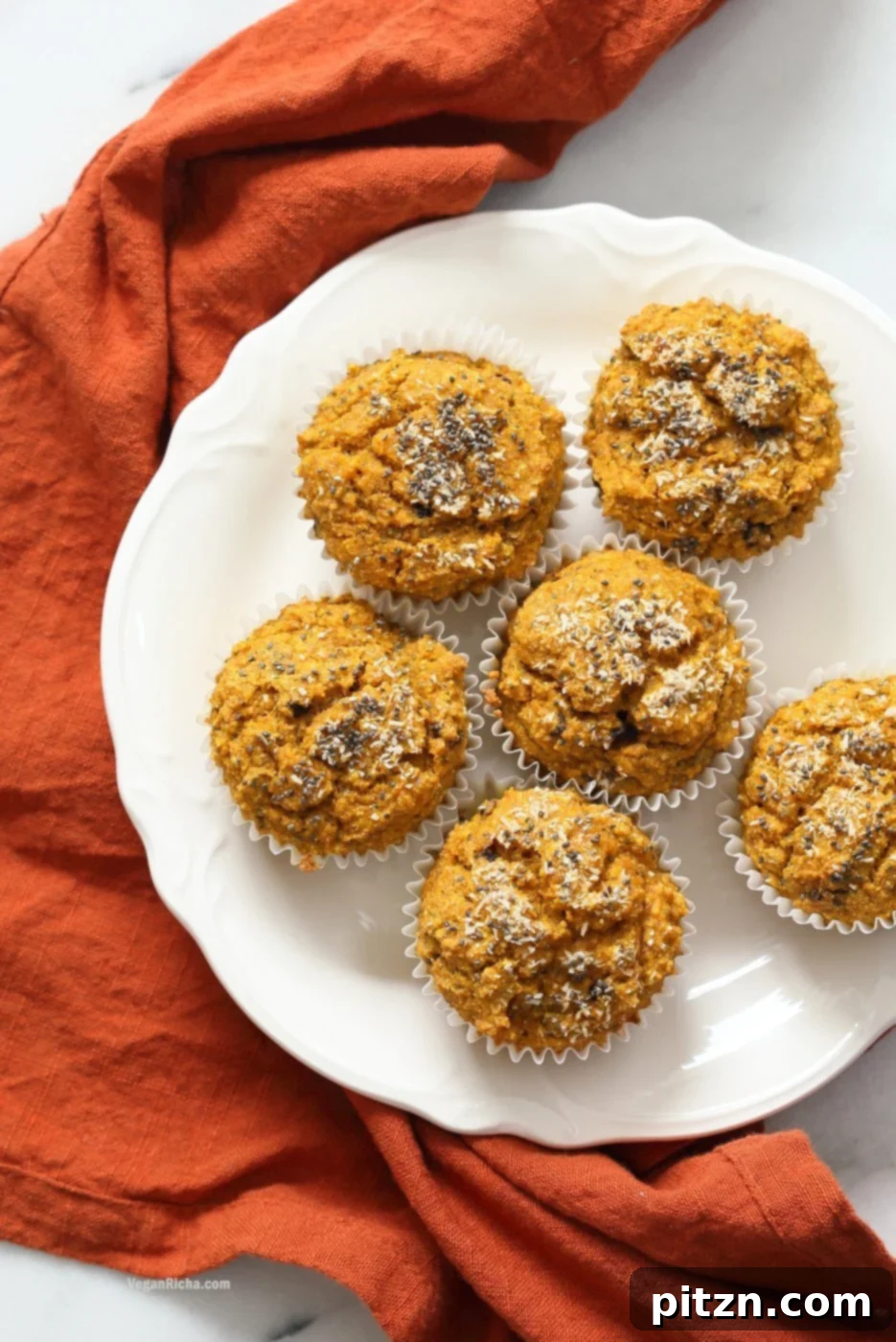 A close-up of delicious Our Vegan Turmeric Carrot Muffins on a white plate, showcasing their golden color and tempting texture