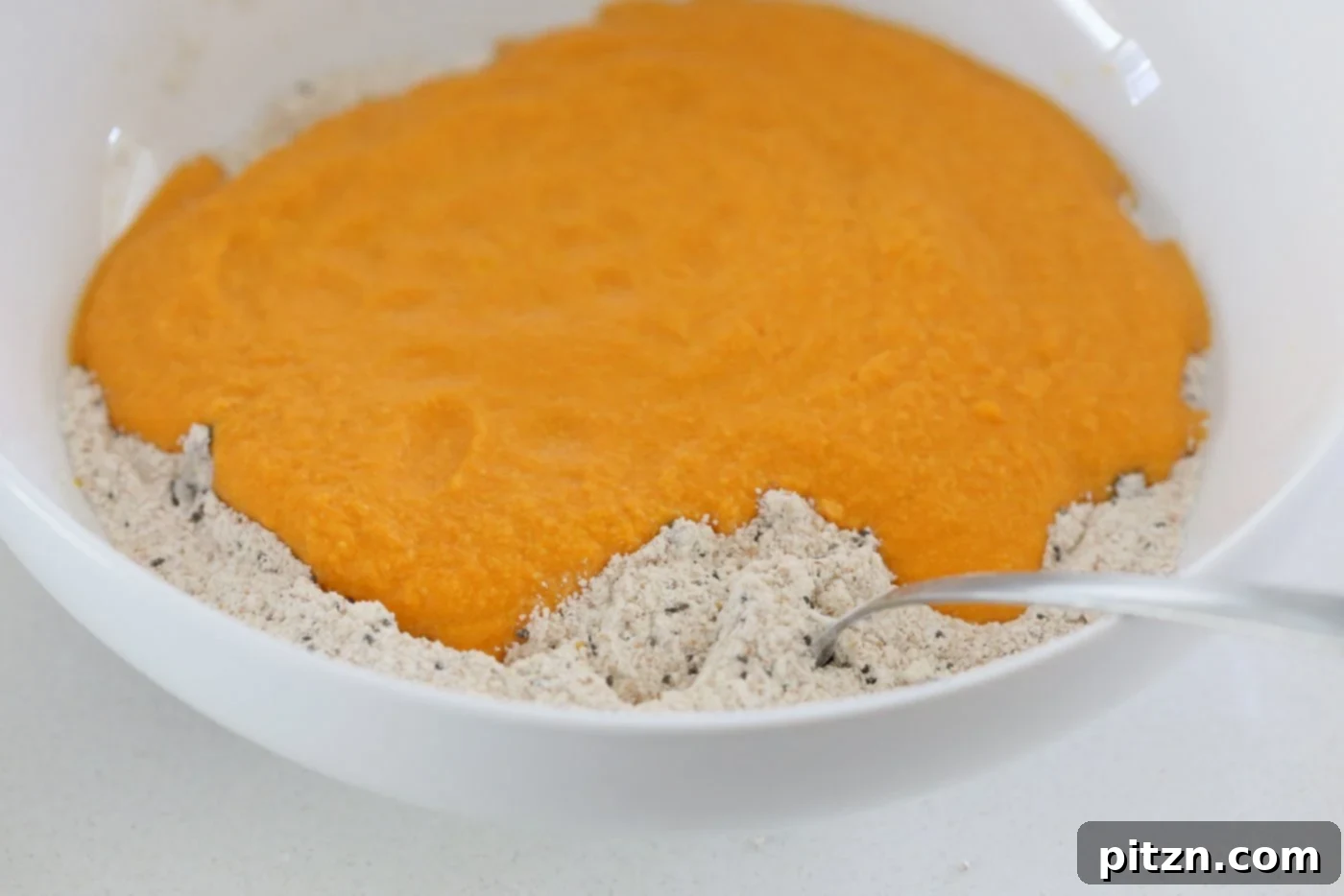 Adding blended wet ingredients to the dry ingredients in a bowl for Our Vegan Turmeric Carrot Muffins, mixing just until combined