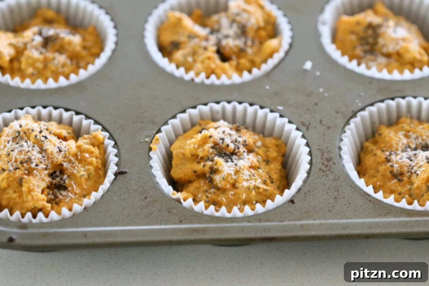 Our Vegan Turmeric Carrot Muffins batter scooped into a lined muffin pan, topped with chia seeds and coconut, ready for baking