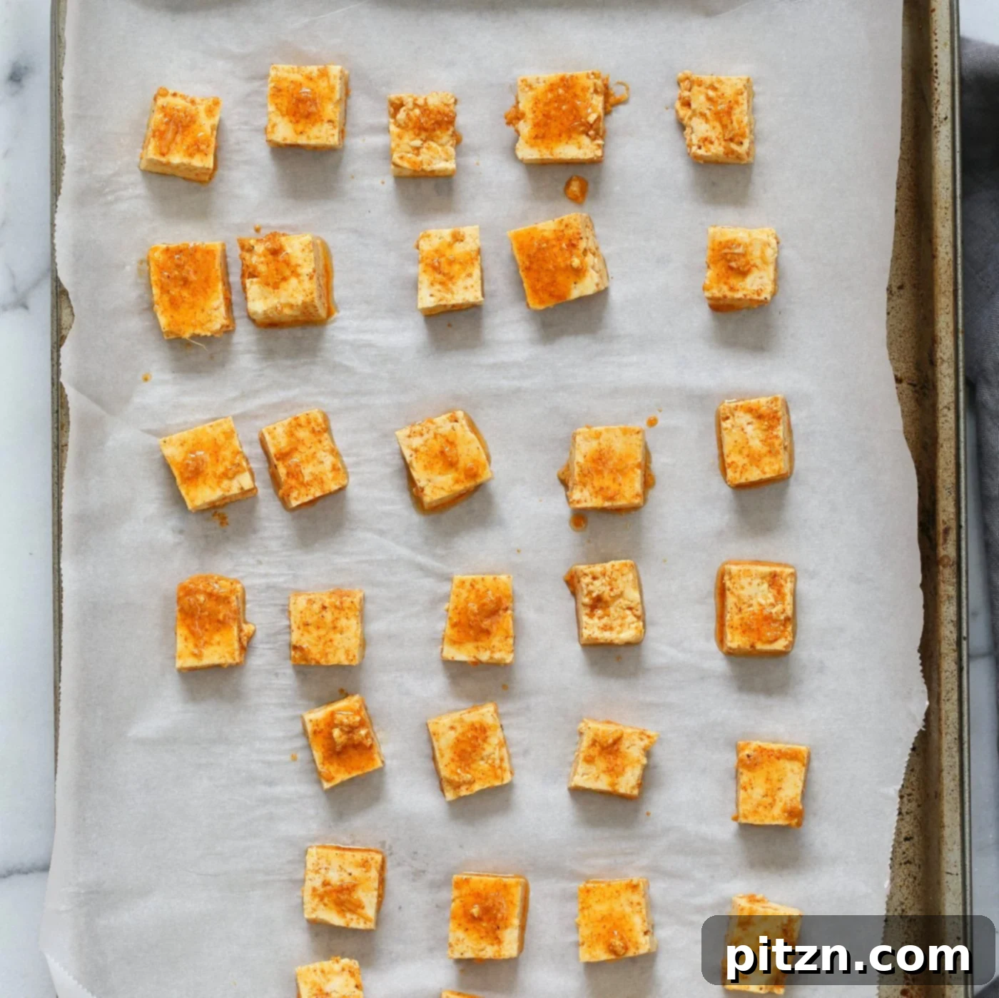 Marinated Tofu cubes on Parchment lined baking sheet ready to be baked for Indian Butter Tofu