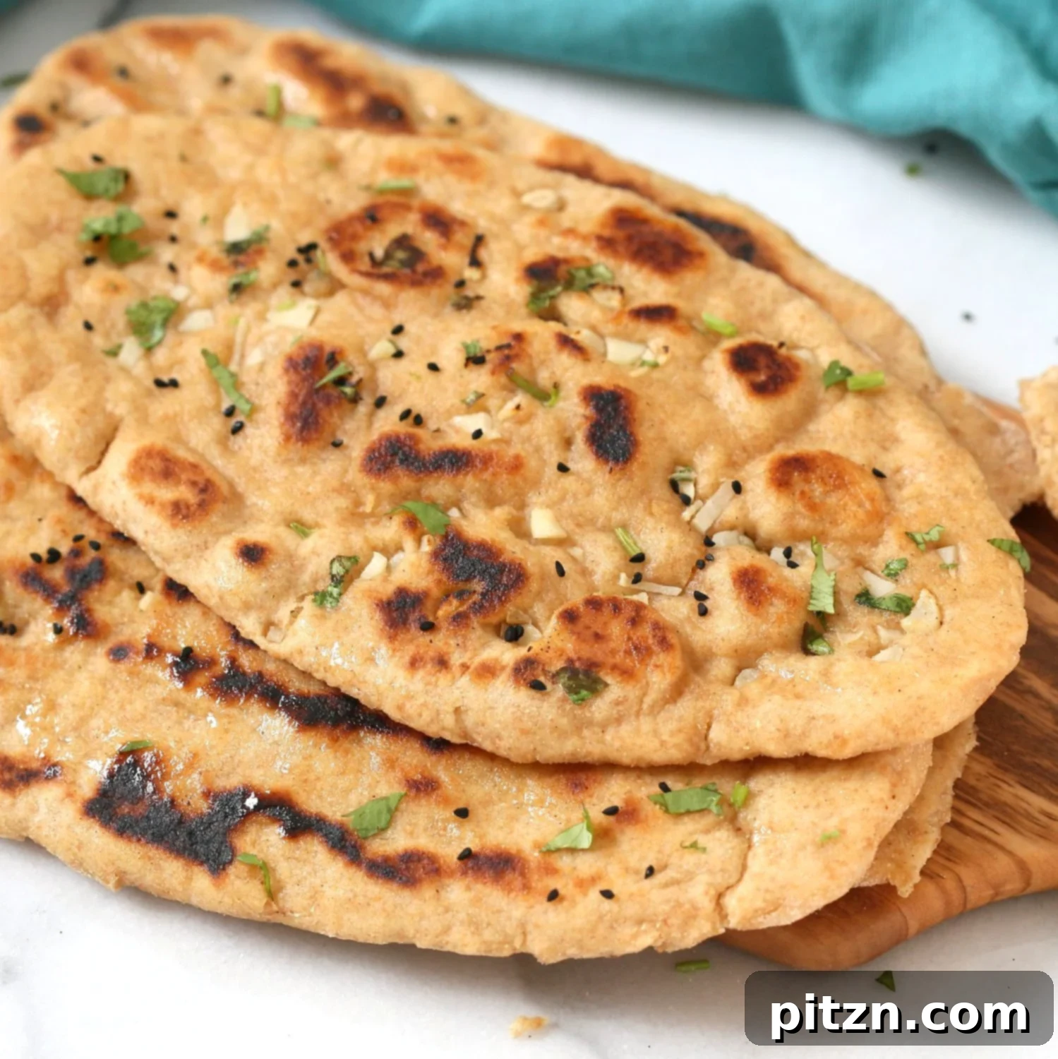 Stack of fluffy Whole Wheat Naan Bread, brushed with vegan butter and garnished with fresh herbs, demonstrating its appealing texture.