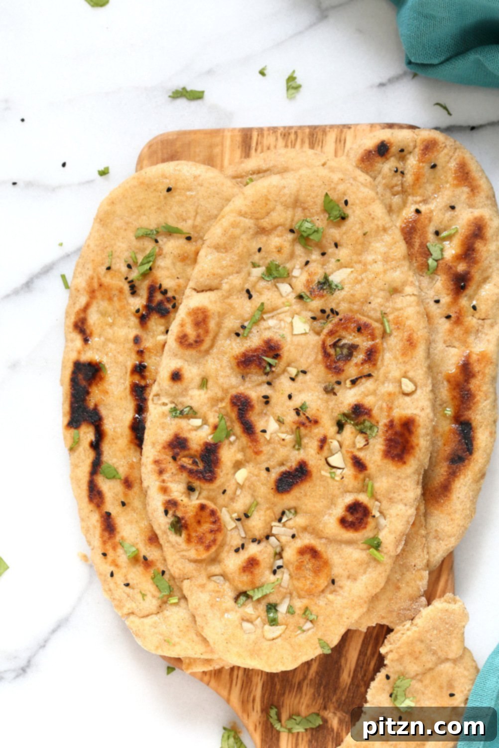 Several pieces of fluffy Whole Wheat Naan Bread on a plate, ready to be served, emphasizing its appealing golden-brown crust.