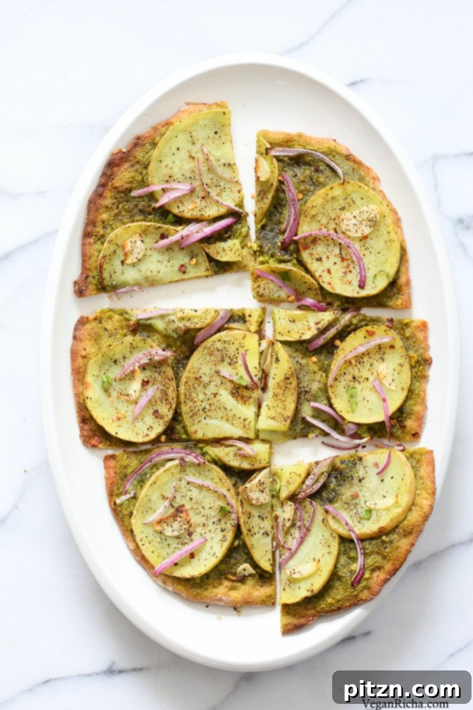 Vegan Basil Spinach Potato Pesto Pizza 5 Freshly baked Easy Potato Pesto Pizza, golden brown and garnished with fresh greens, ready to be sliced and served.