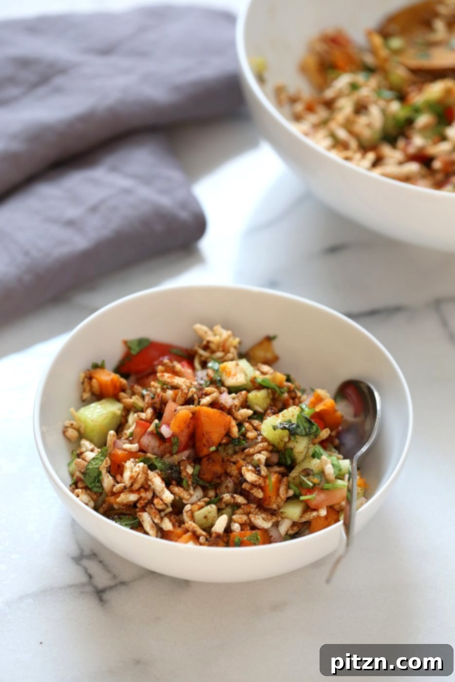 A fresh bowl of Sweet Potato Bhel, an Indian street food snack salad, featuring crisp puffed rice, soft sweet potato, and vibrant herbs like mint and cilantro, all dressed in a tangy tamarind chutney. This vegan, gluten-free, and nut-free recipe is quick to prepare. VeganRicha.com