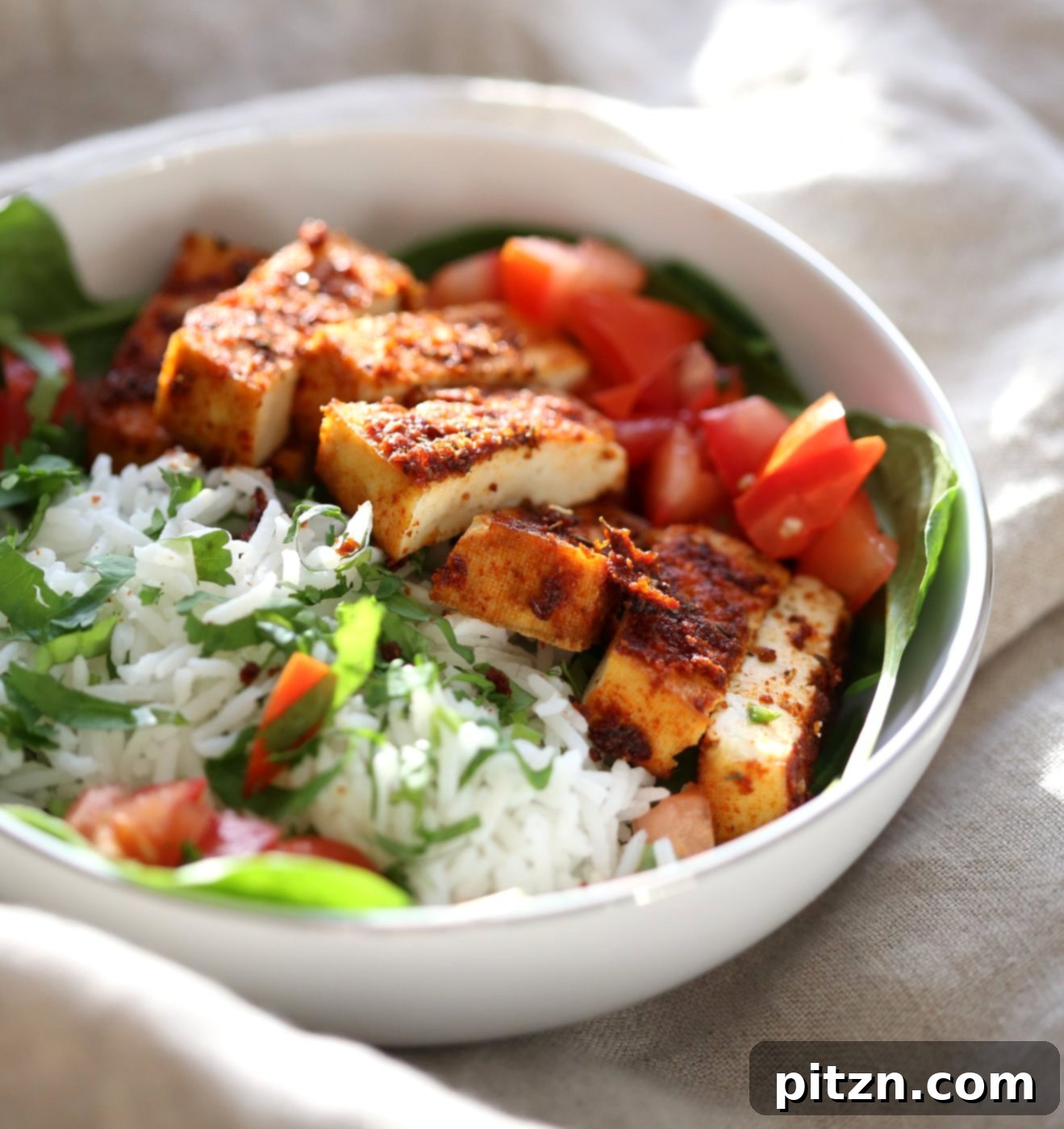 Close-up of freshly baked Cajun Tofu slices arranged on a bed of vibrant Cilantro Lime Rice, alongside crisp greens and bright red tomatoes, highlighting the dish's fresh ingredients.