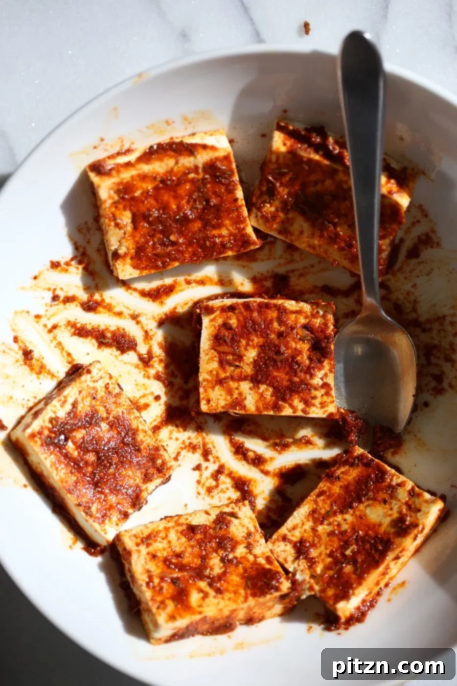 Close-up of uncooked firm tofu being rubbed with a homemade Cajun spice paste, lime juice, and olive oil, ready for baking.